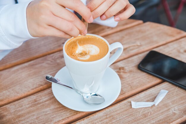 Vrouw zet suiker in kopje met latte