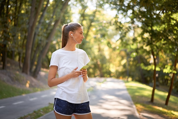 Vrouw zetten oortelefoons om muziek te luisteren voordat joggen zomer park