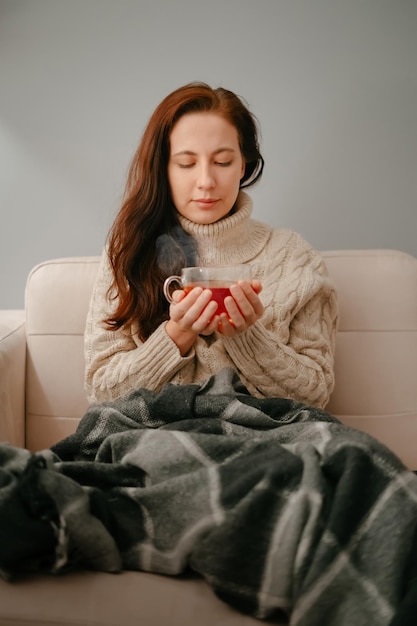 Vrouw ziek van de griep zit thuis hete thee te drinken om de winter op te warmen