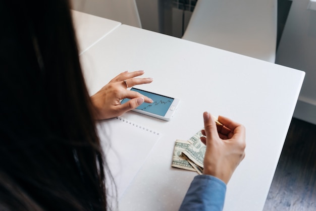 Vrouw zit aan tafel en kijkt naar de grafiek op de achtergrond van geld op tafel