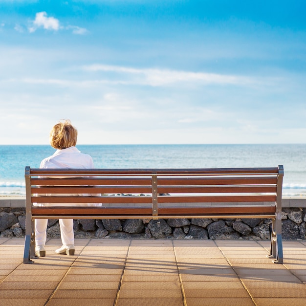 Vrouw zit alleen in een bankje, kijkend naar de zee