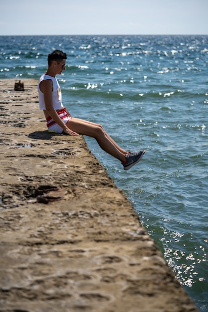 Vrouw zit alleen op de pier in korte broek en hemd met schoenen. Achteraanzicht. Zomer zee