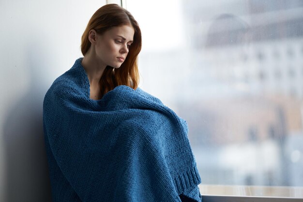 Vrouw zit bij het raam met een blauwe geruite glimlach thuis Foto van hoge kwaliteit