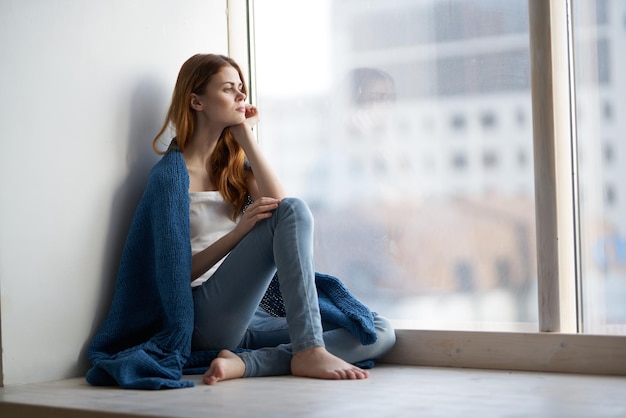 Vrouw zit bij het raam met een blauwe geruite glimlach thuis