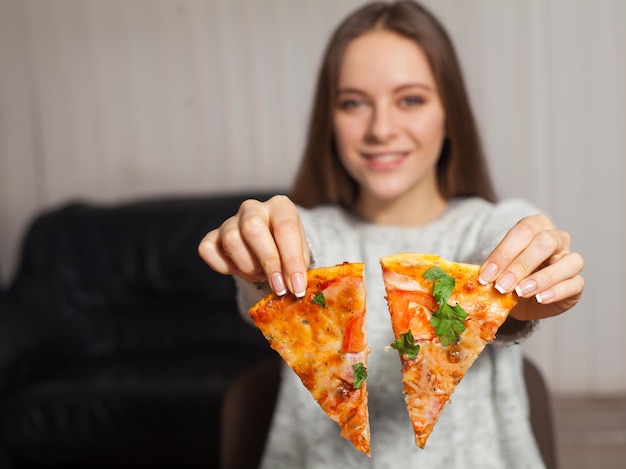 Vrouw zit en houdt twee sneetjes pizza in haar handen