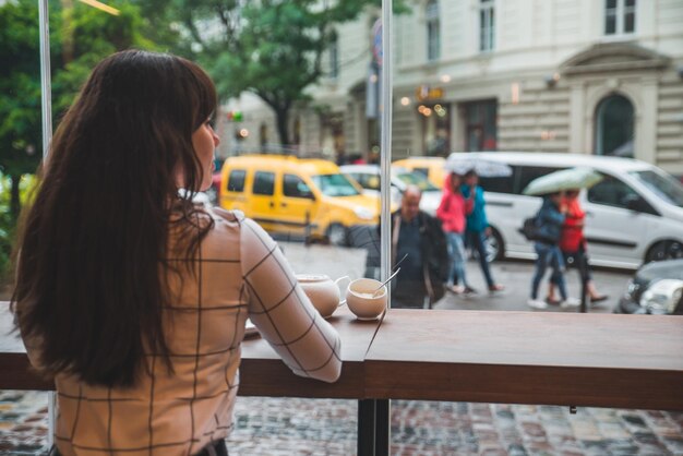 Vrouw zit in café met groot glazen raam en prachtig uitzicht op straat in de stad