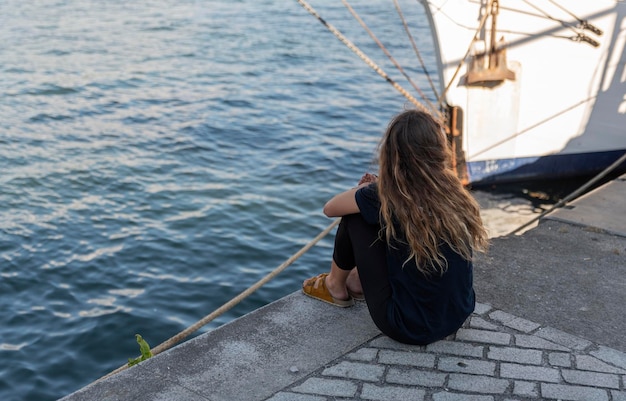 Vrouw zit in de haven en kijkt naar de zee