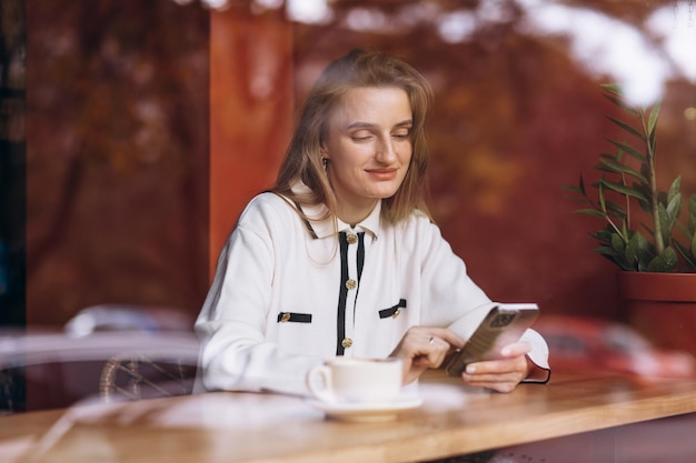 Vrouw zit in een koffietentje met een mobiele telefoon