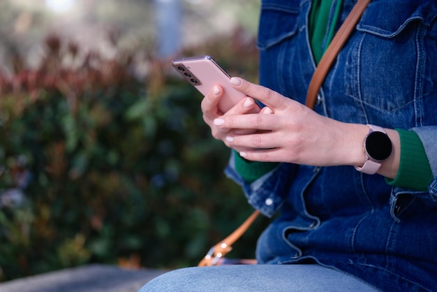 Vrouw zit in het park en houdt mobiele telefoon in haar handen close-up communicatie op afstand in