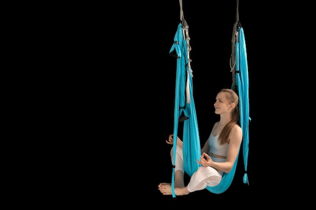 Vrouw zit in lotushouding in hangmat en oefent luchtyoga op zwarte achtergrond kopieer ruimte antigravity yoga