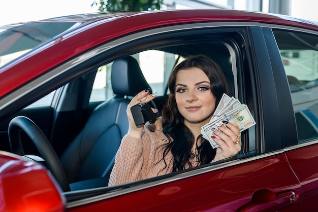 Vrouw zit in nieuwe auto en toont dollars en sleutels