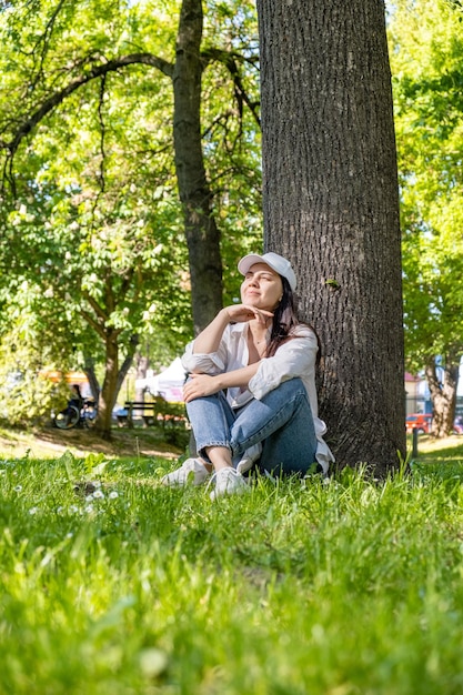 Vrouw zit onder de boom in het stadspark en surft op internet aan de telefoon