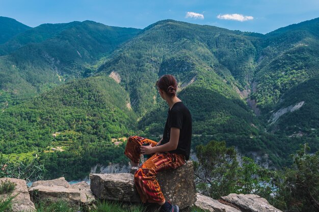 Foto vrouw zit op de berg en kijkt naar de bergen.