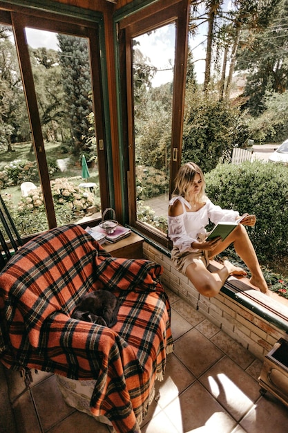 Foto vrouw zit op de vensterbank terwijl ze een boekfoto leest