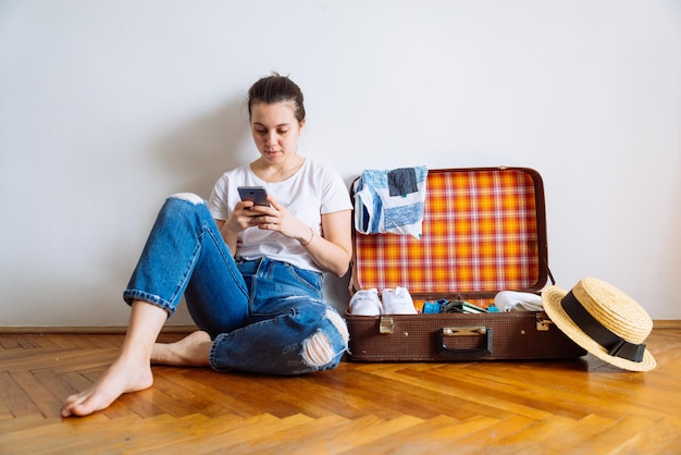 Vrouw zit op de vloer met kleding voor het inpakken van een mobiele telefoon voor de kopieerruimte van het reisreisconcept