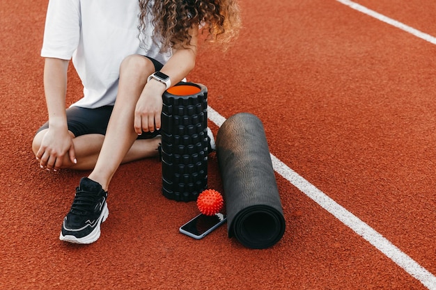 Vrouw zit op een atletiekbaan met de apparatuur voor training en zelfmassage.