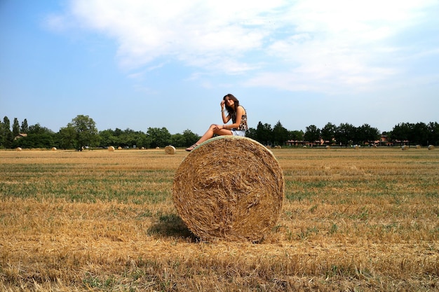 Foto vrouw zit op een hooibal op het veld tegen de lucht