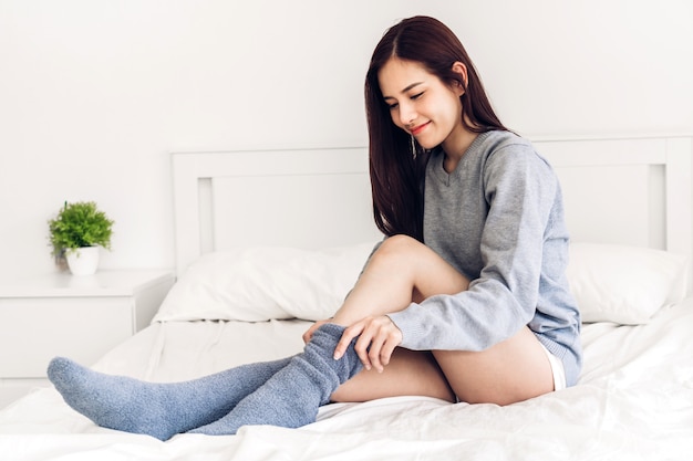 Vrouw zit op het bed dragen en het aantrekken van lange warme sokken in koude winterdag