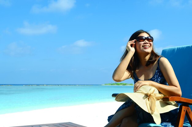 Vrouw zit op het strand tegen de blauwe hemel.