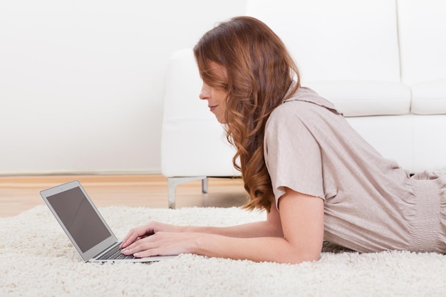 Vrouw zit op het tapijt met een laptop