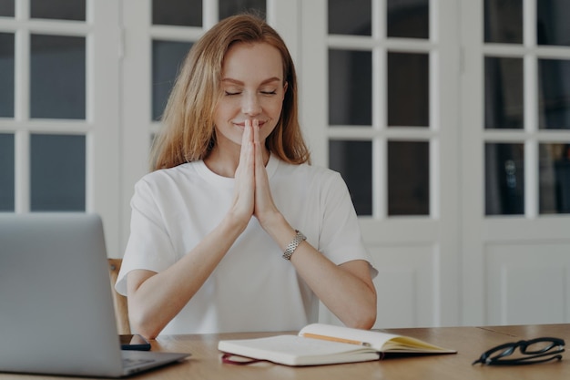 Vrouw zit op laptop met gevouwen handpalmen mediteren controle emotionele toestand pauzeren in het werk