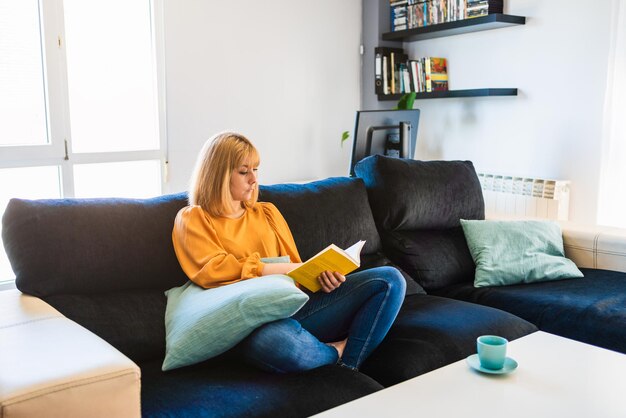 Vrouw zit thuis een boek op de bank te lezen