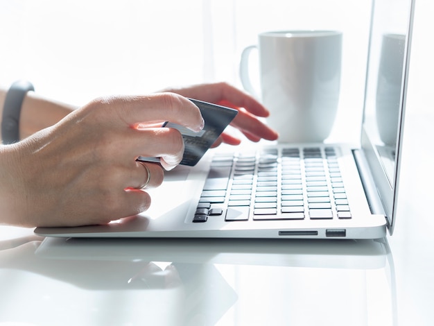 Foto vrouw zitten aan een tafel, het drinken van thee en kijken naar een laptop, betalen voor aankopen