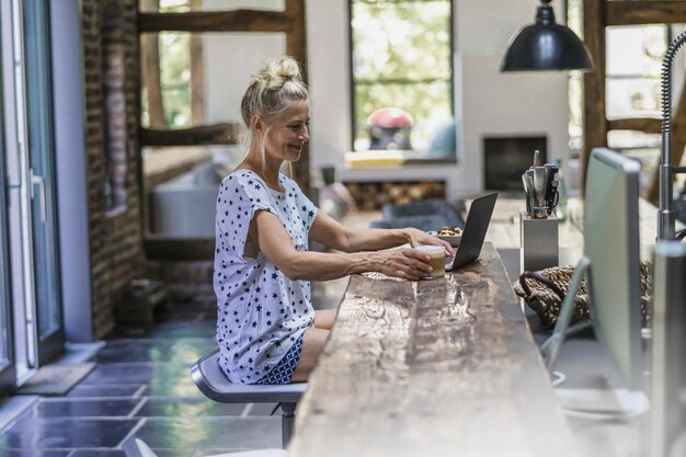 Foto vrouw zitten in de keuken, met behulp van laptop