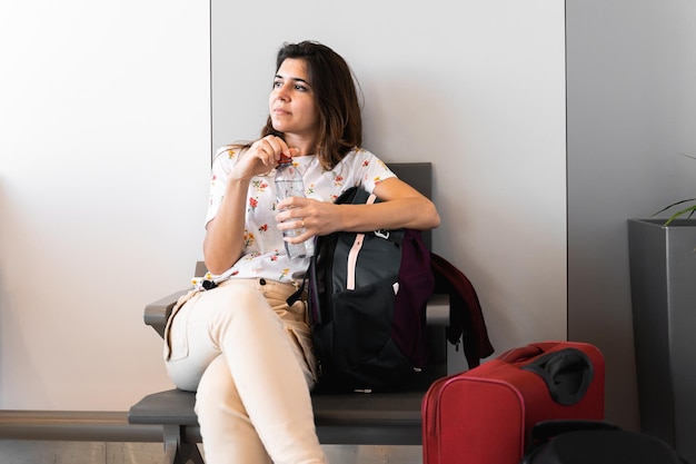 Vrouw zittend in een stoel in de vertreklounge met veel tassen en bagage wachtend op de vlucht