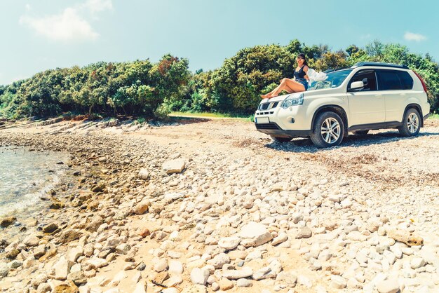 Vrouw zittend op auto kap bij zomer strand vakantie concept