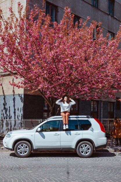 Vrouw zittend op de auto bloeiende sakura boom op achtergrond lente komt eraan