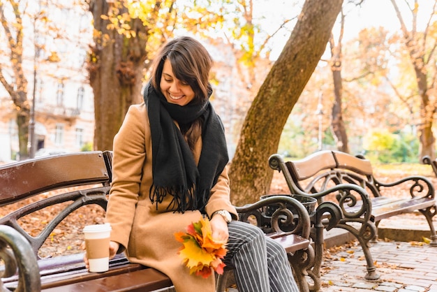 Vrouw zittend op de bank in het herfststadspark koffie drinken