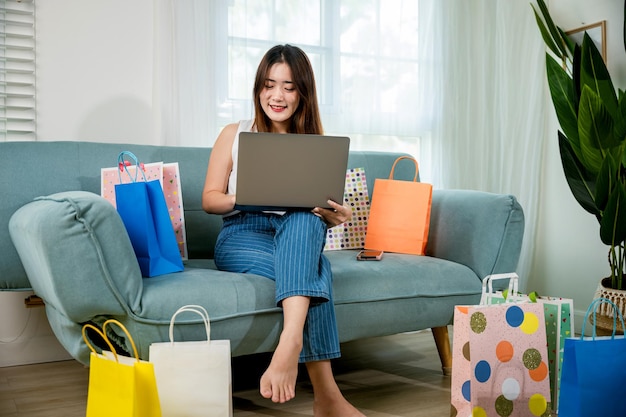 Vrouw zittend op de bank met boodschappentassen laptopcomputer gebruiken om online te winkelen