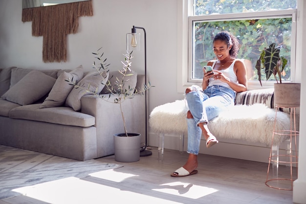 Vrouw zittend op de bank thuis kijken naar mobiele telefoon