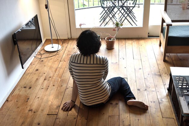 Vrouw zittend op de houten vloer kijkend naar het raam