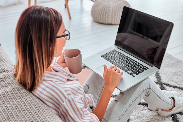 Vrouw zittend op de vloer met koffiemok bezig met laptopcomputer Van bovenaf fotograferen Ruimte kopiëren