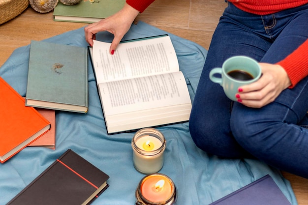 Vrouw zittend op de vloer van haar huis met een kopje koffie in haar hand een boek lezend bij kaarslicht