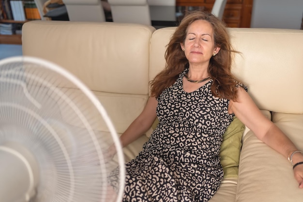 Vrouw zittend op een bank met een grote ventilator ervoor die haar frisse lucht geeft van de hoge temperaturen