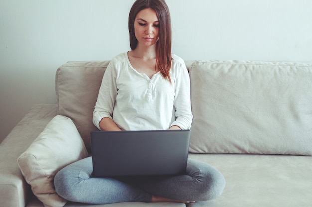 Vrouw zittend op een bank thuis en met behulp van laptop.