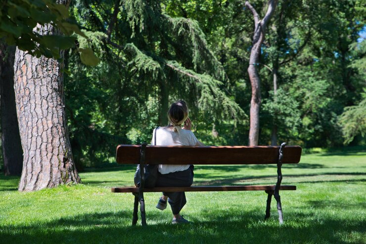 Vrouw zittend op een bankje in het park praten op haar mobiele telefoon op een zonnige dag
