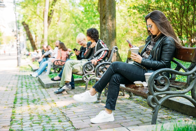 Vrouw zittend op een bankje in het stadspark koffie drinken op internet surfen via mobiel