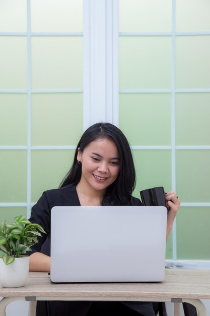 Vrouw zittend op een stoel met laptop aan tafel met een drinkglas en kijkend naar het scherm