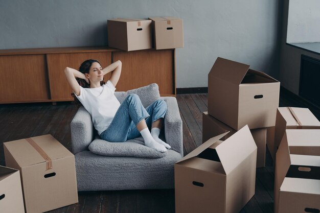 Vrouw zittend op fauteuil ontspant tijdens het inpakken van dozen op verhuisdag naar nieuw huis Eenvoudige verhuizing