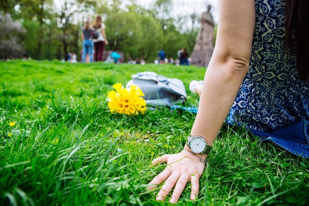 Vrouw zittend op gras in stadspark met gele bloemen