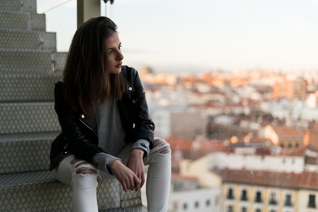 Vrouw zittend op trappen met luchtfoto van een grote stad