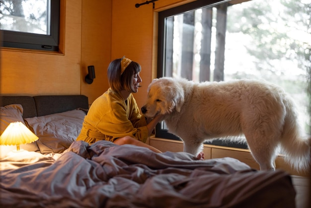 Vrouw zorgt voor haar hond terwijl ze in bed ligt in een kleine slaapkamer van een houten hut op de natuur