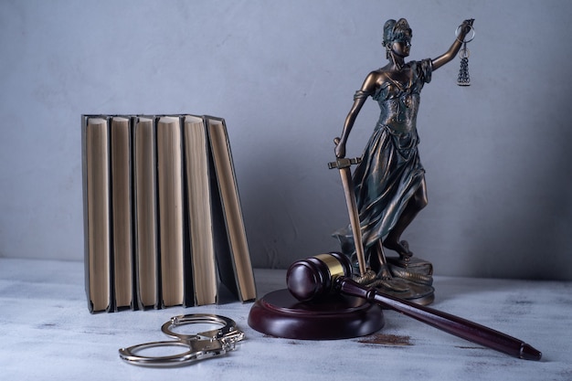 Vrouwe justitia, rechtershamer, boeken, handboeien op een oude houten tafel