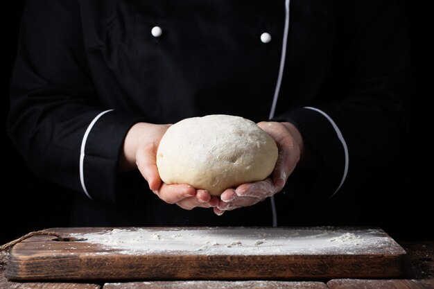 Vrouwelijk de gistdeeg van de chef-kokholding in haar handen op zwarte achtergrond.