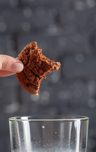 Vrouwelijk hand dunking koekje in melk dicht omhoog