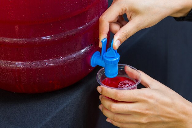 Vrouwelijk het waterglas van de handholding met rode vloeibare drankachtergrond